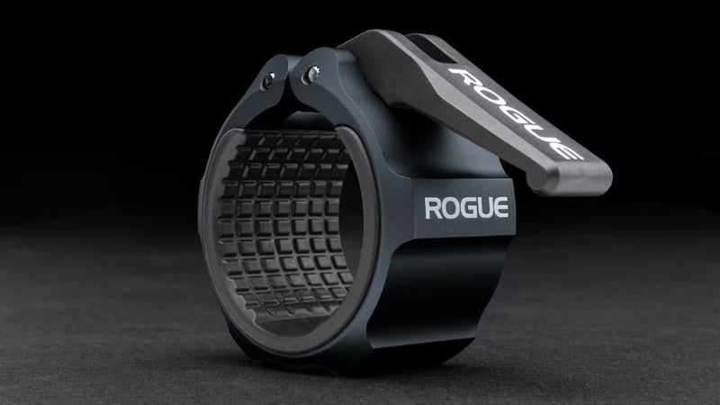 ROGUE USAアルミニウムカラー 2.0 ダークネイビーを斜め前方から捉え、ロックオープンナイロンレバーとCNC加工アルミボディ、内側ラバーライニング構造が確認できるオリンピックバーベル用カラー