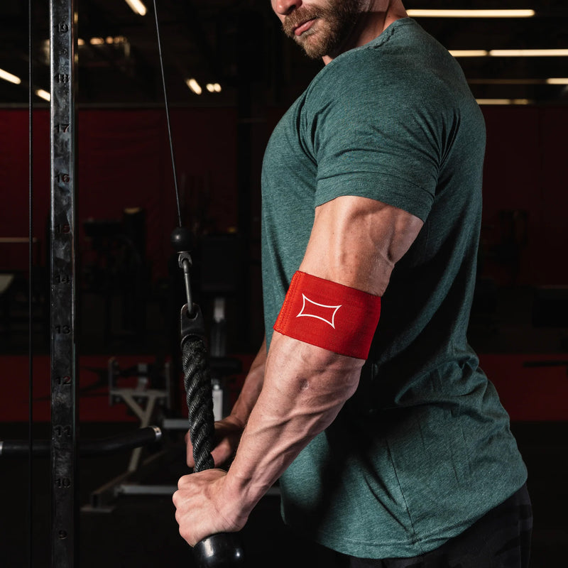 SLINGSHOT コンプレッションカフ2.0 レッドを装着した腕を斜め前方から撮影。ケーブルマシン使用時の肘サポート部位と伸展状態が確認できる構図