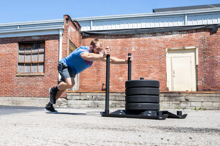 ROGUE エコードッグ スレッド ブラックを屋外で使用し、前方から押し出す動作を横方向から捉えた構図。スピード＆アジリティー向けの実践的な使用シーン。