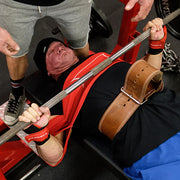 SLINGSHOT オリジナルスリングショット レッドを装着しベンチ上でバーベルを下ろす場面を上方から捉え、胸部と上腕の連動や高重量時の反発サポートが分かる使用シーン