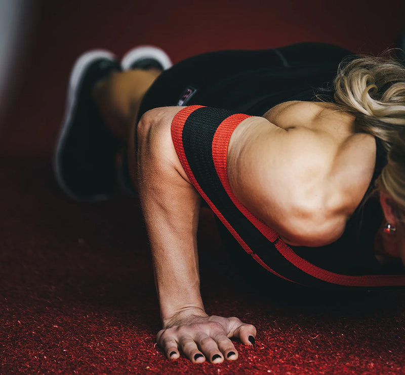 SLINGSHOT スリングショットプッシュアップ レッド＆ブラックを装着した側面寄り視点。床に近い角度から上腕と肩周りのフィット感と負荷分散が分かる構成。