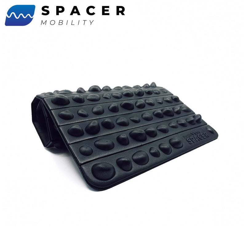 黒のROCK MATを斜め前から見た状態で、折り畳み可能な構造と表面に配置された多数の突起形状が分かる構成により、全体フォルムと厚みのバランスを確認できるモビリティ用フットケアマット