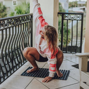 黒のROCK MATの上に立った状態を側面から捉え、足裏で突起を踏みながら体重を乗せてバランスを取る様子が分かる構図で、使用時の荷重位置を想定しやすい使用シーン