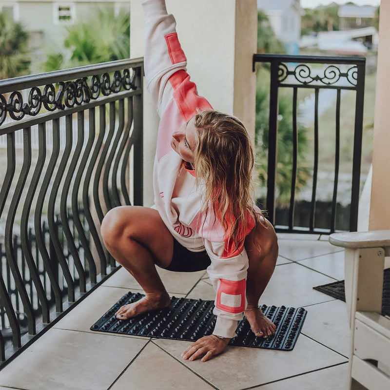 黒のROCK MATの上に立った状態を側面から捉え、足裏で突起を踏みながら体重を乗せてバランスを取る様子が分かる構図で、使用時の荷重位置を想定しやすい使用シーン