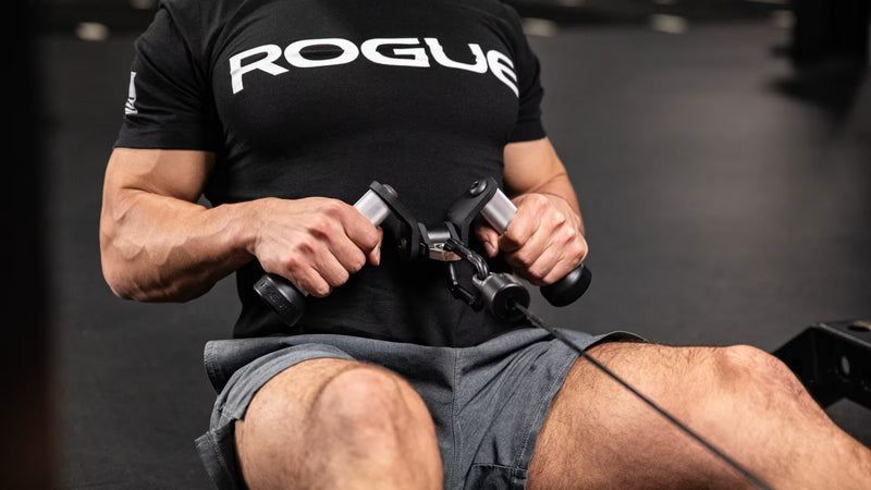 シルバーのROGUE Vグリップ ケーブルアタッチメントを使用し、シーテッドローの収縮姿勢を正面から捉えた上半身の使用例