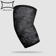 SLINGSHOT ストロング エルボースリーブ ブラックカモの単体製品を斜め前方から捉えた構図。肘全体を覆う立体形状とカモ柄デザイン、ロゴ位置が分かる視点